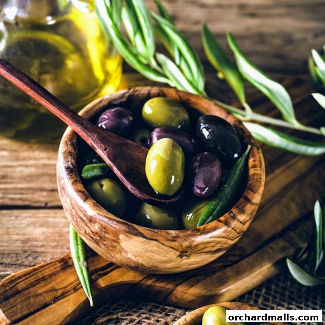 A wooden bowl filled with assorted olives and a wooden spoon, with olive oil in the background.