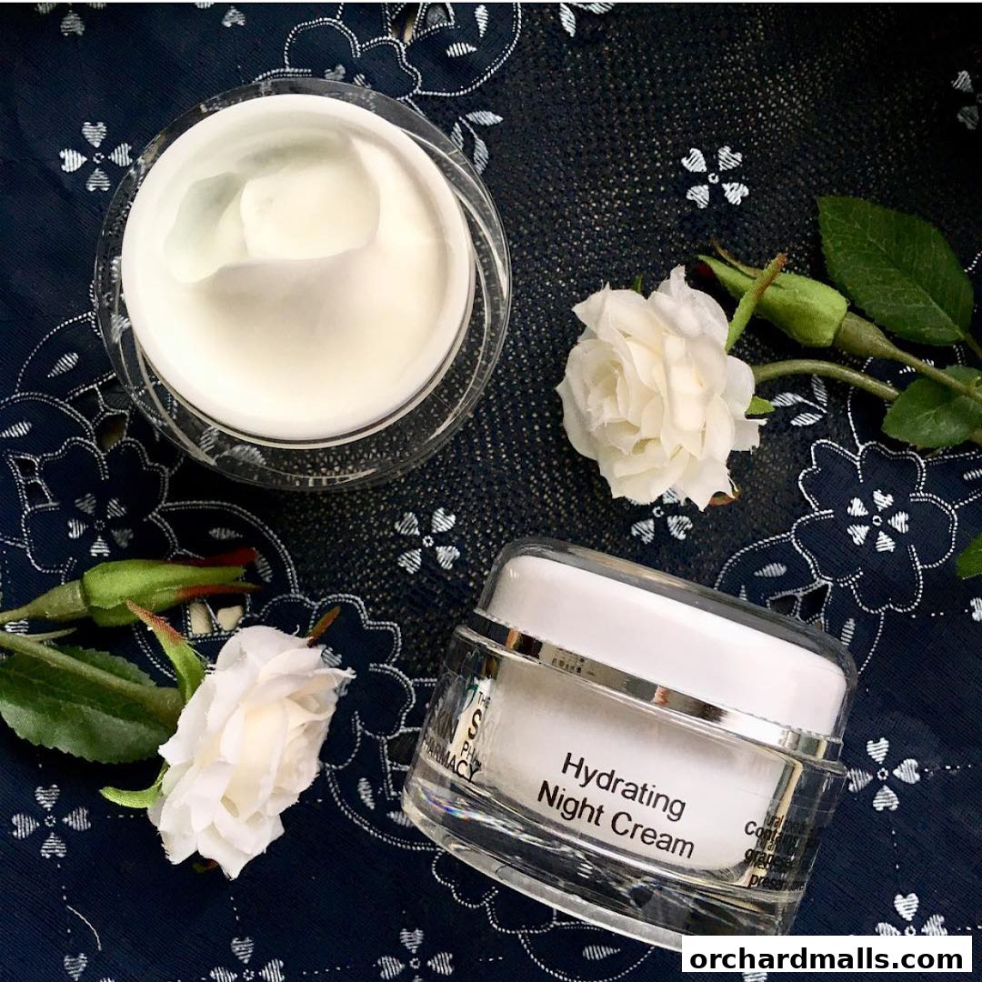 Two jars of skincare products, one open, with white roses on a dark patterned cloth.