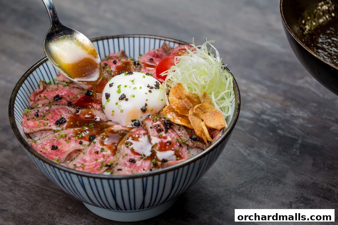 A close-up of a delicious beef donburi bowl with a poached egg and sauce being drizzled.
