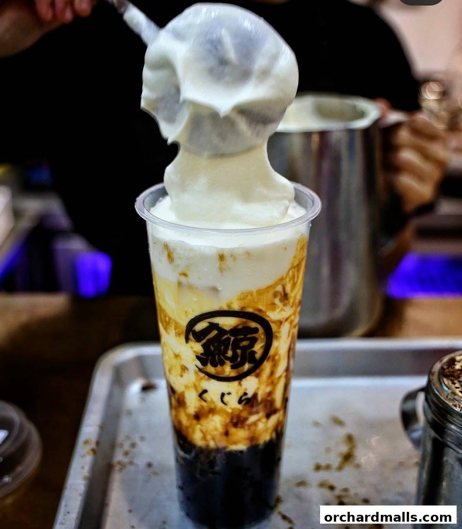 A creamy topping is being added to a layered brown sugar bubble tea.