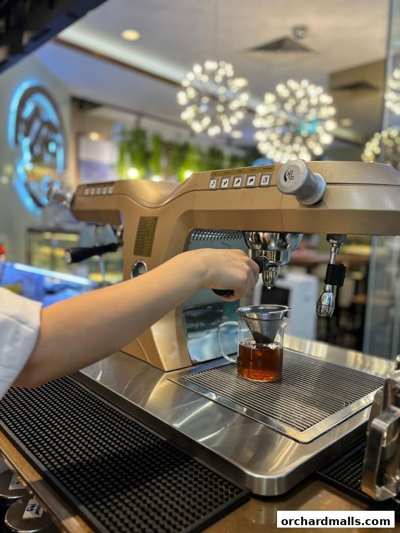 A barista prepares a drink using a golden espresso machine and a pour-over setup.