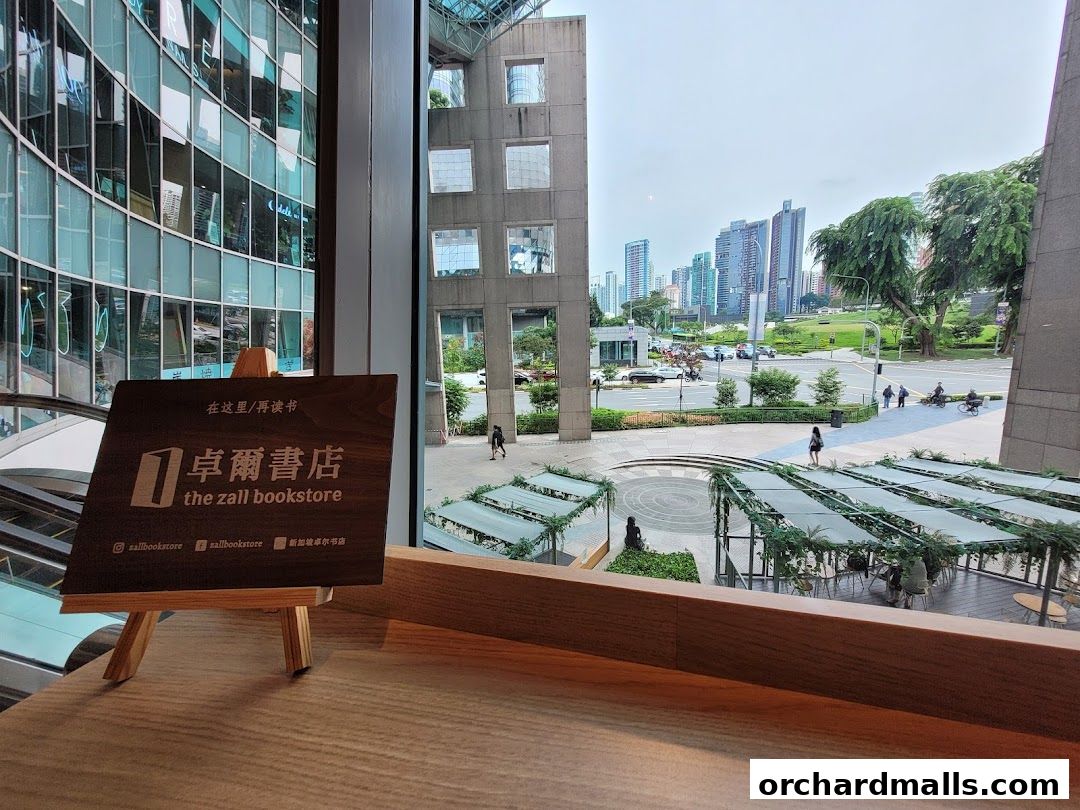 A wooden sign for The Zall Bookstore is displayed on a table, with a city view in the background.