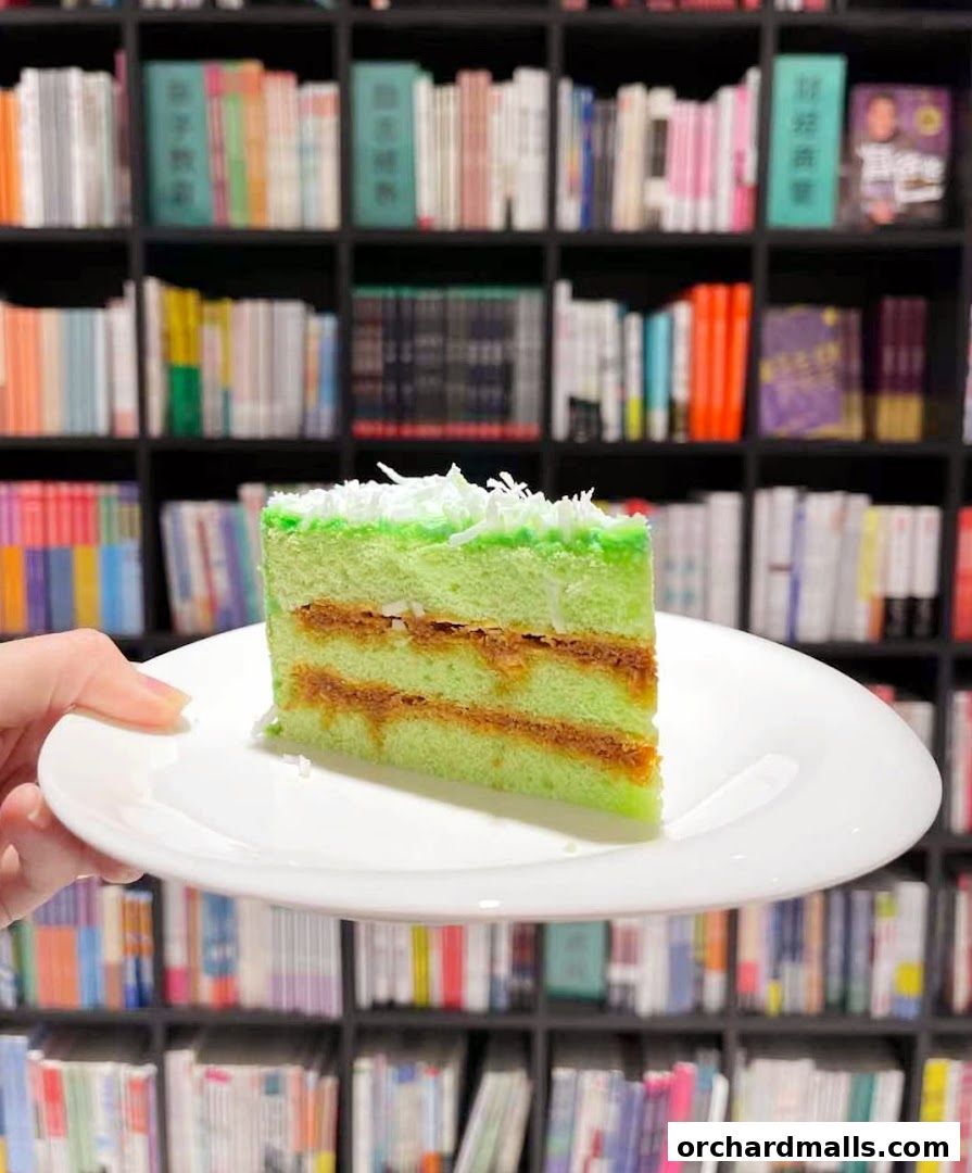 A slice of green cake with coconut flakes on top, served on a white plate.