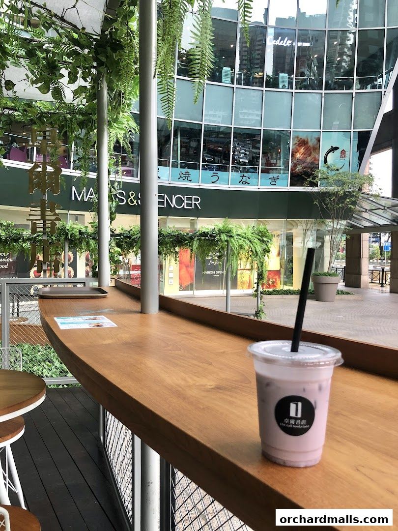 A drink sits on a wooden counter with a bookstore logo, overlooking a mall with M&S.