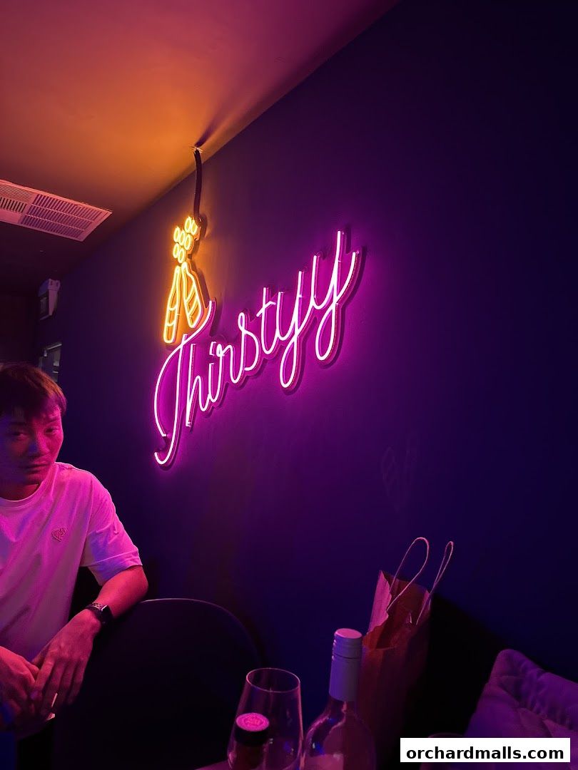 A neon sign spelling 'Thirstyy' with a ballet shoe graphic on a dark wall.