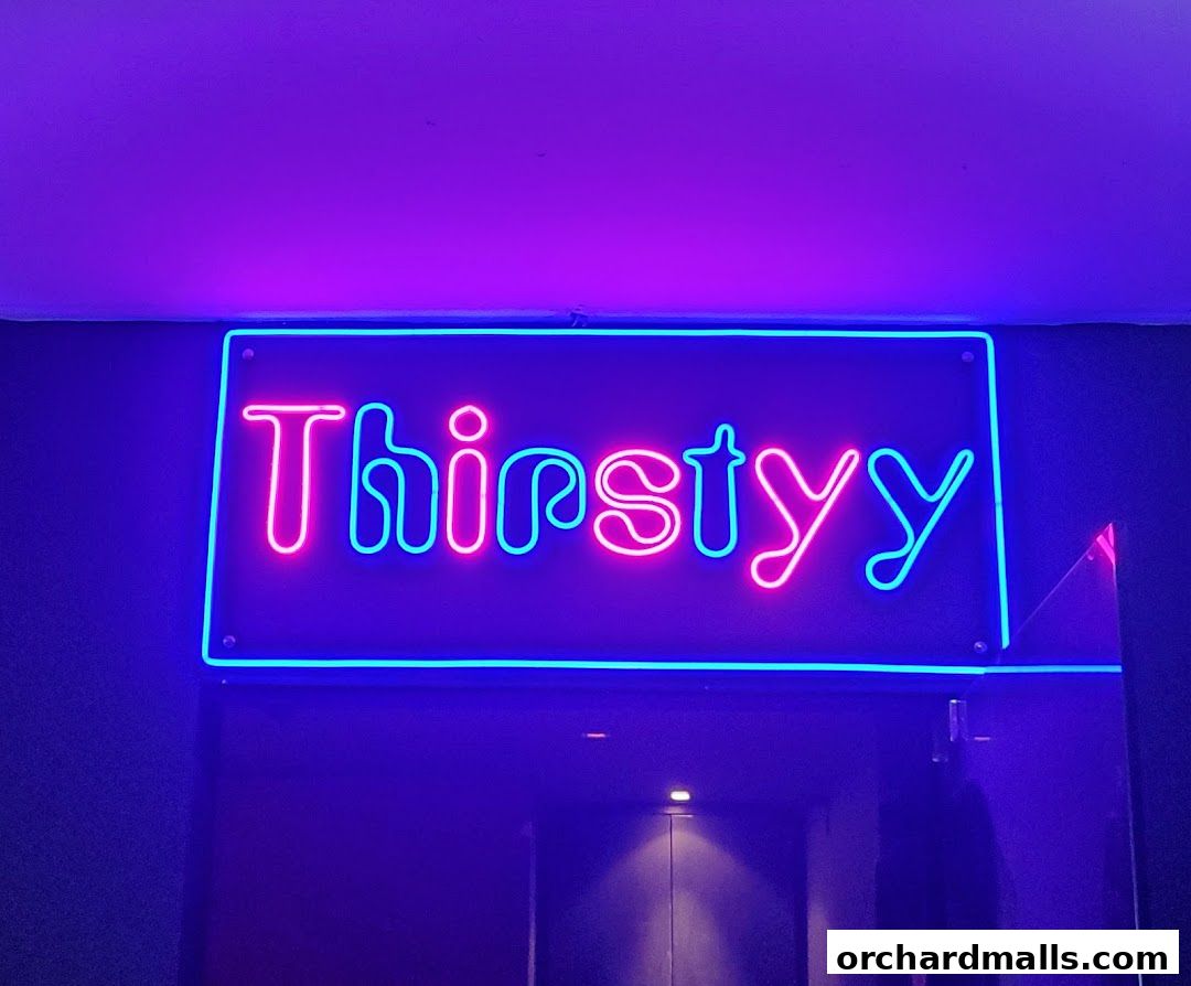 A neon sign for 'Thirstyy' glows in pink and blue, above a dark entrance.