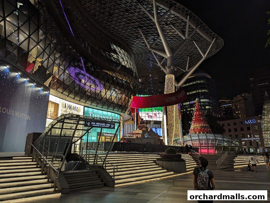 A nighttime view of a modern shopping complex featuring Louis Vuitton, Dior, and Tiffany & Co. stores.