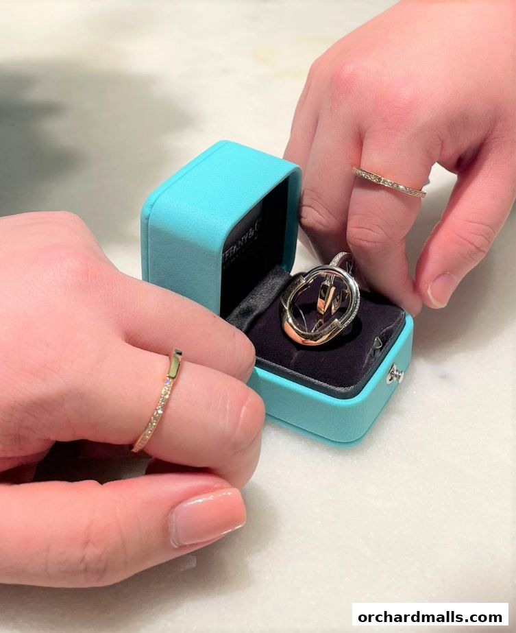 Hands holding a Tiffany & Co. jewelry box with a pendant and rings.