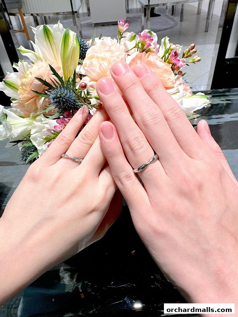 Two hands wearing Tiffany & Co. rings, with a floral arrangement in the background.