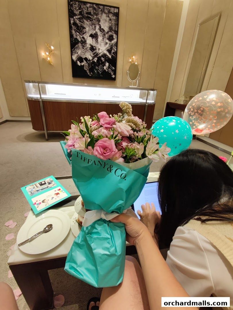 A person is using a tablet next to a bouquet of flowers and balloons in a Tiffany & Co. store.