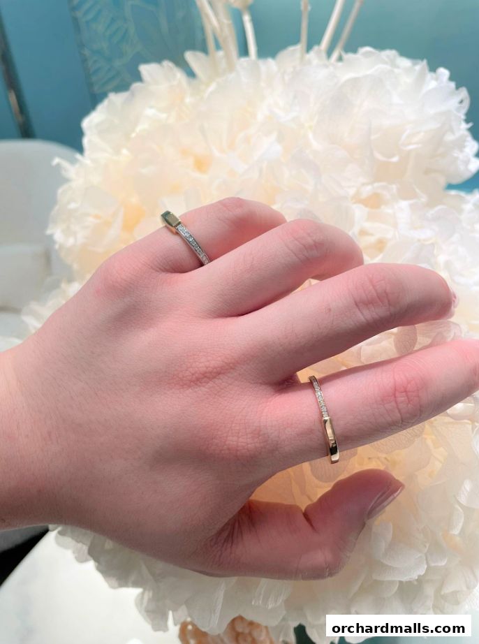 A hand wearing two delicate diamond-studded rings against a soft, floral background.