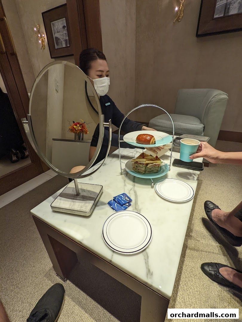 A server offers a pastry and coffee to guests at a table in a luxurious setting.