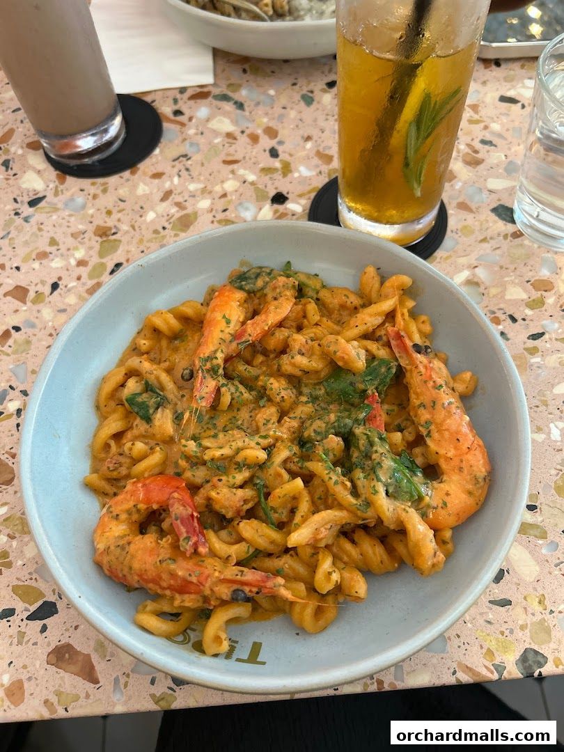 A close-up of a creamy pasta dish with shrimp and herbs, served with drinks.