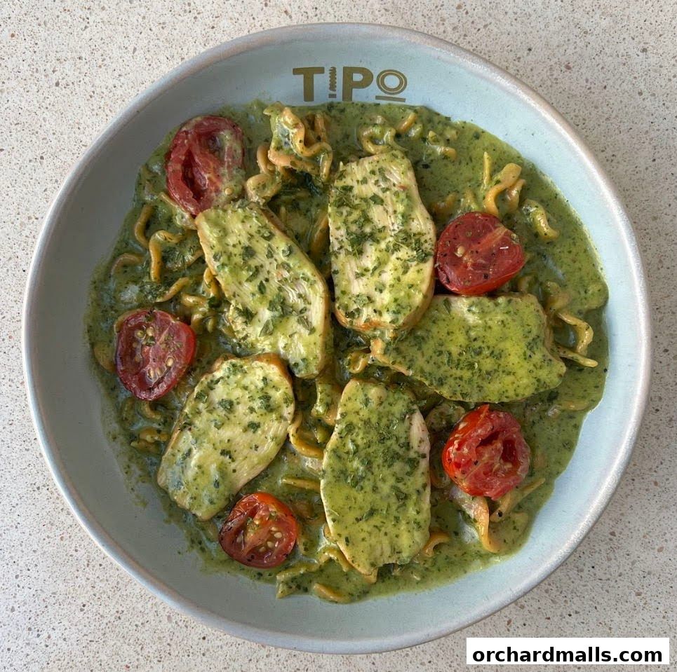 A bowl of pasta with chicken, cherry tomatoes, and a creamy green sauce.