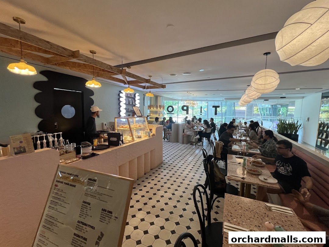 Interior of a busy cafe with people dining at tables and a counter with pastries.