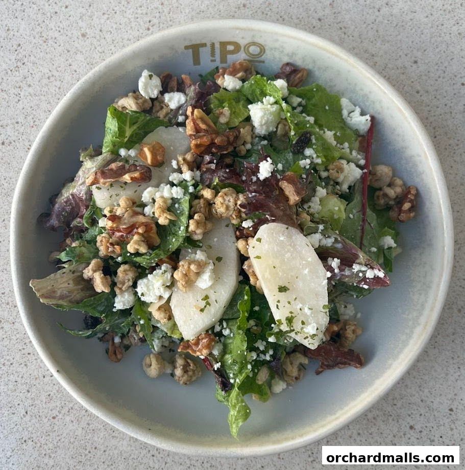 A close-up of a fresh salad with greens, cheese, nuts, and fruit in a bowl.