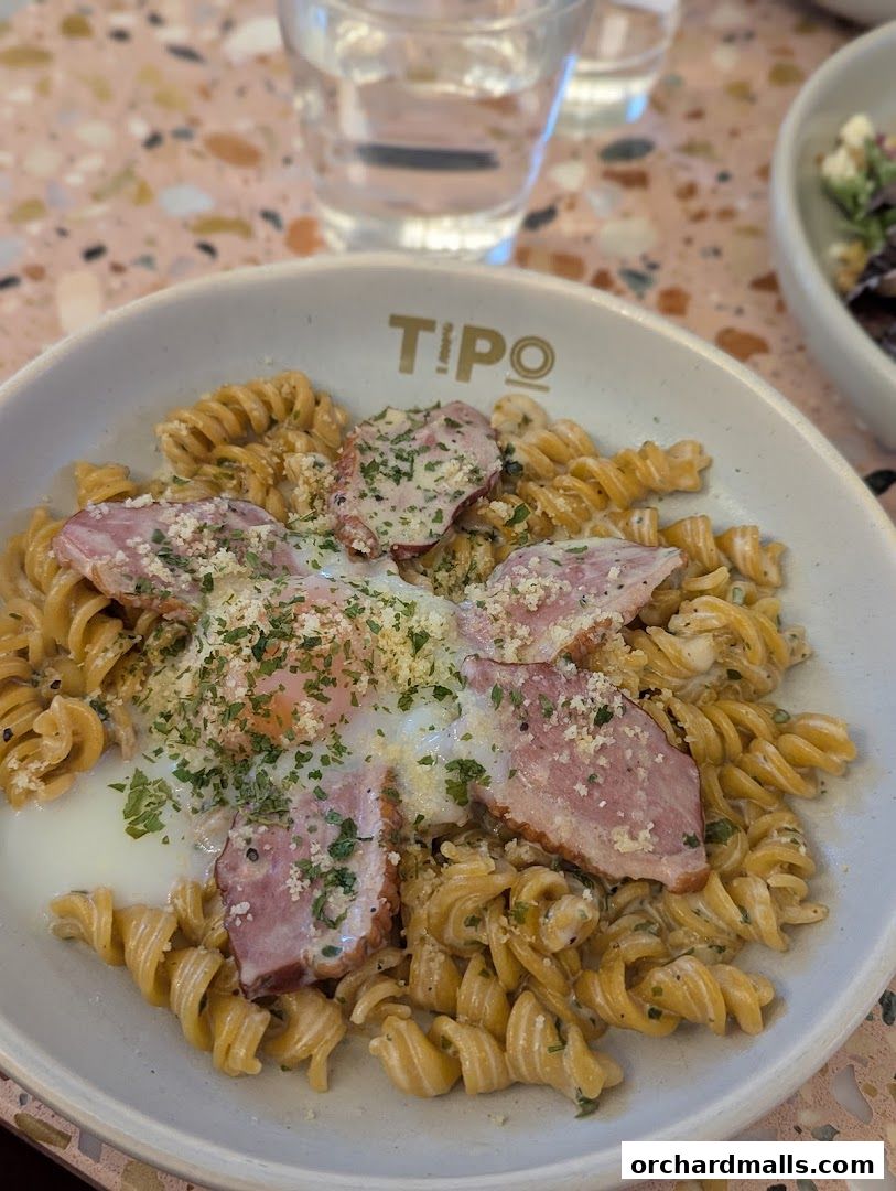 A bowl of pasta with egg and meat, garnished with herbs and cheese.