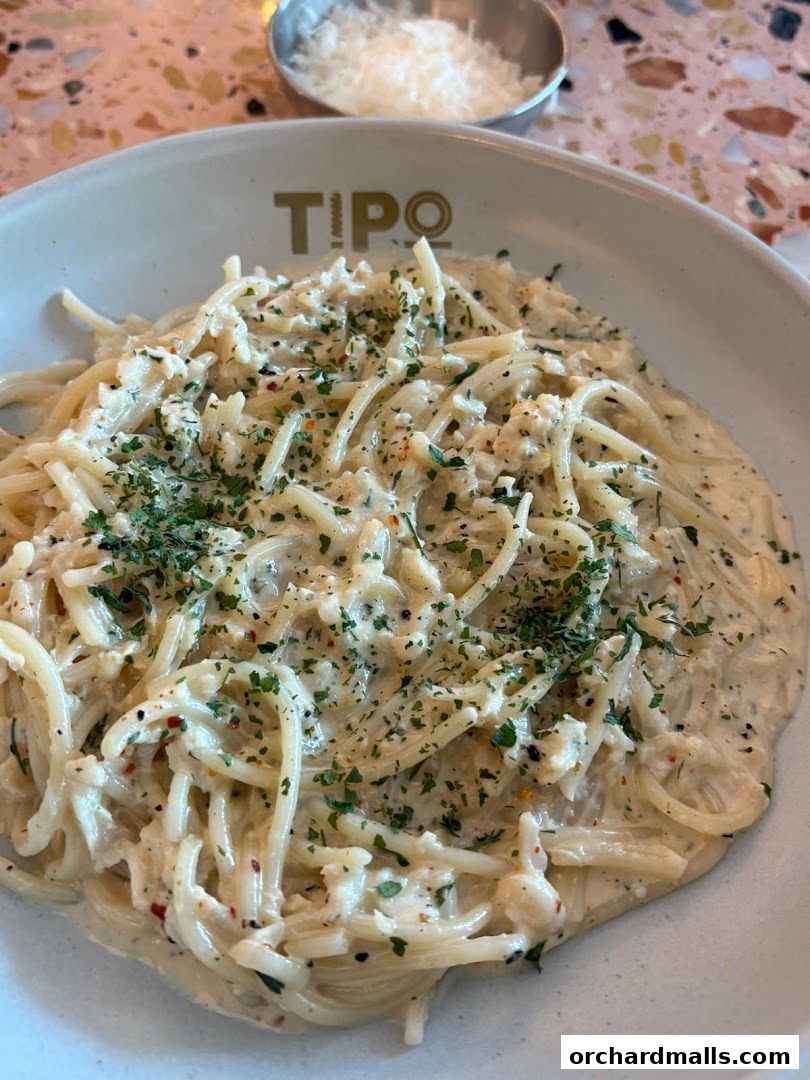 A close-up of a creamy pasta dish topped with shredded cheese and herbs.
