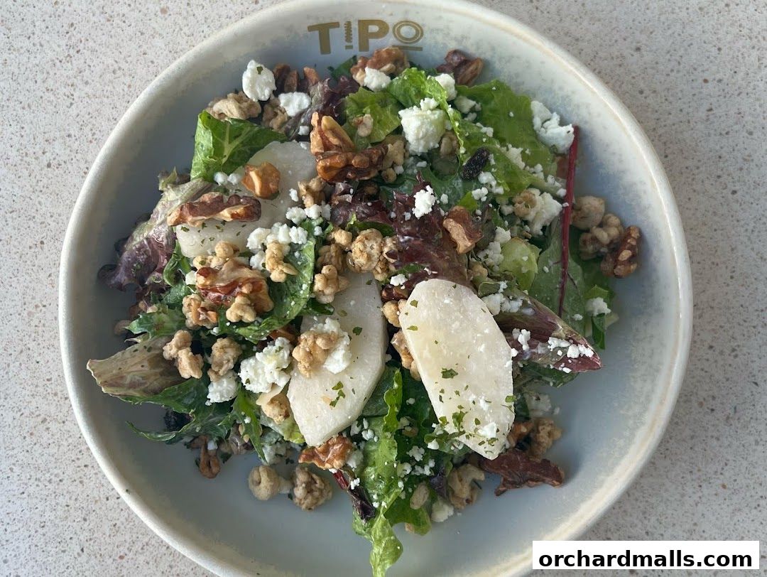 A close-up of a fresh salad with cheese, nuts, and fruit in a bowl.