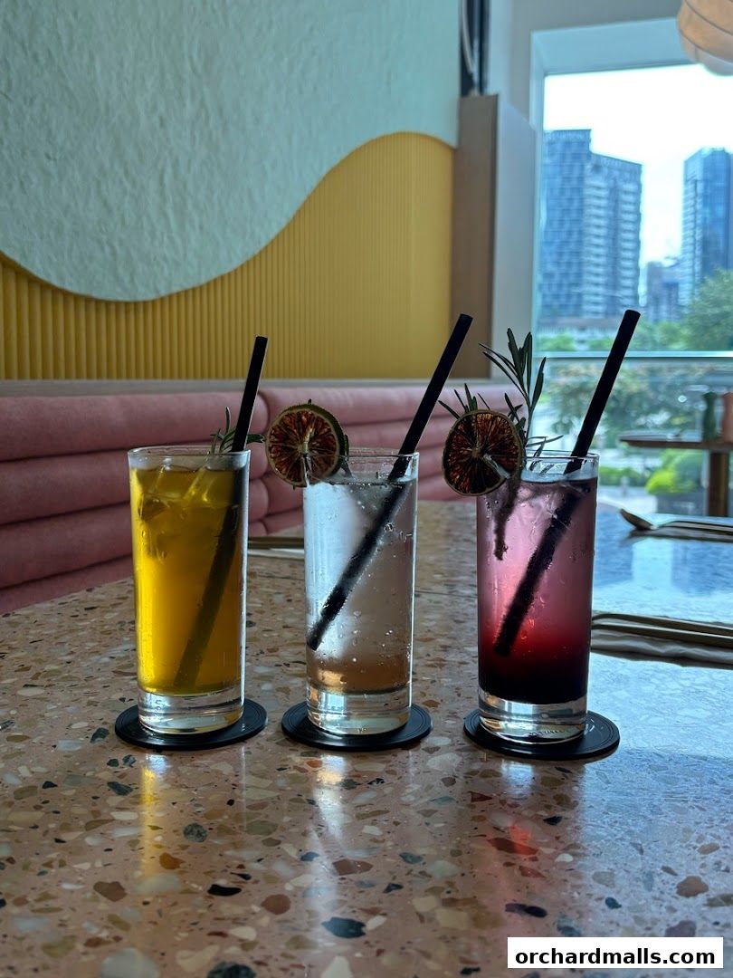 Three colorful drinks with garnishes and straws on a terrazzo table.