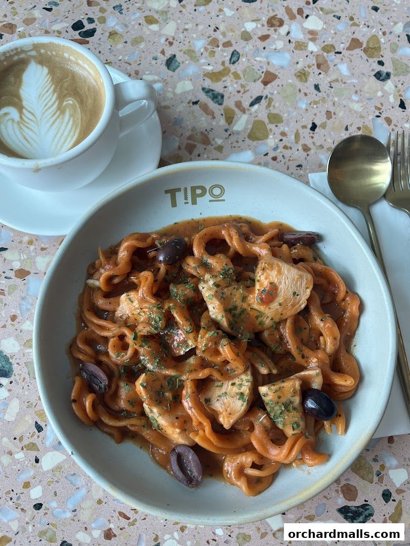 A bowl of pasta with chicken and olives, served with a latte.