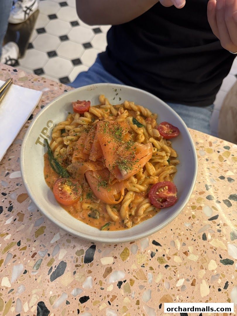 A bowl of pasta with smoked salmon and cherry tomatoes on a terrazzo table.