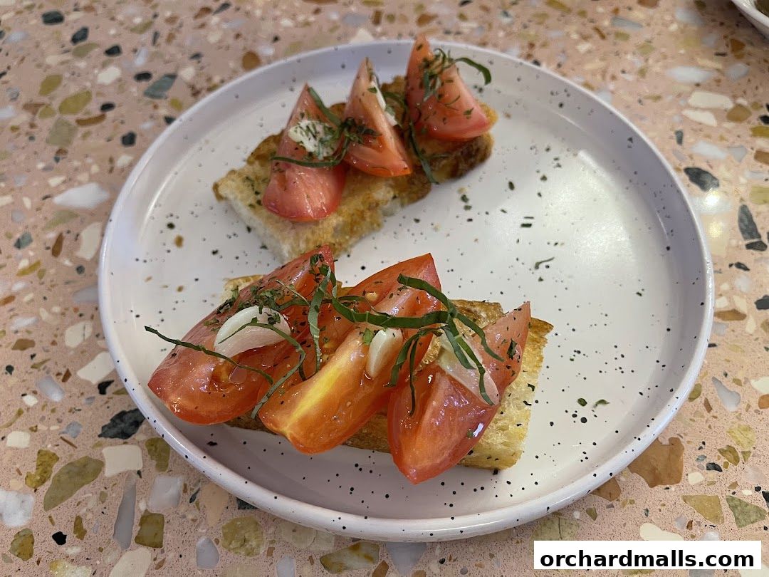A plate of tomato bruschetta with fresh basil and garlic on a speckled terrazzo table.