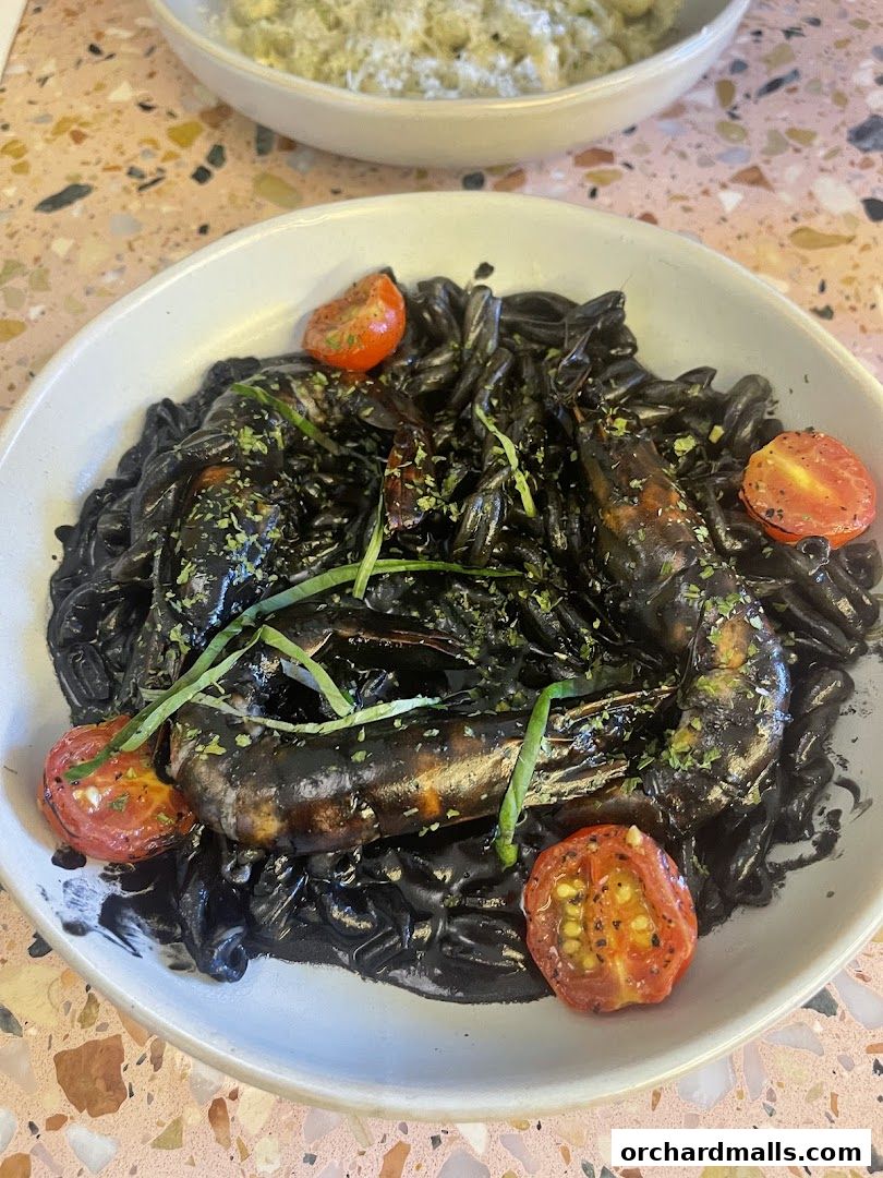 A close-up of a black pasta dish with prawns and cherry tomatoes.