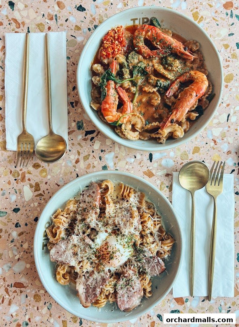 Two bowls of pasta with shrimp and bacon, served with golden cutlery.