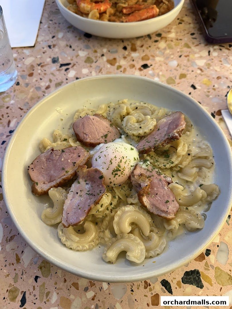 A close-up of a pasta dish with sliced meat and a poached egg, garnished with herbs.