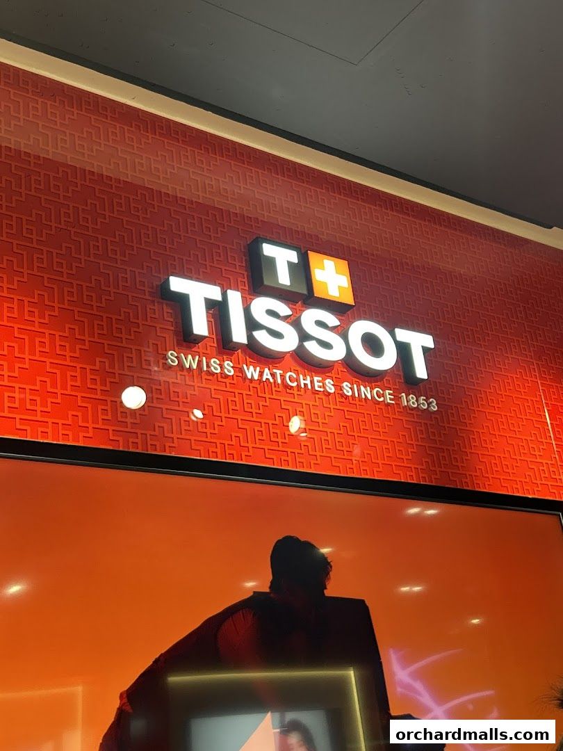 The Tissot logo and slogan are displayed on a red patterned wall above a display.