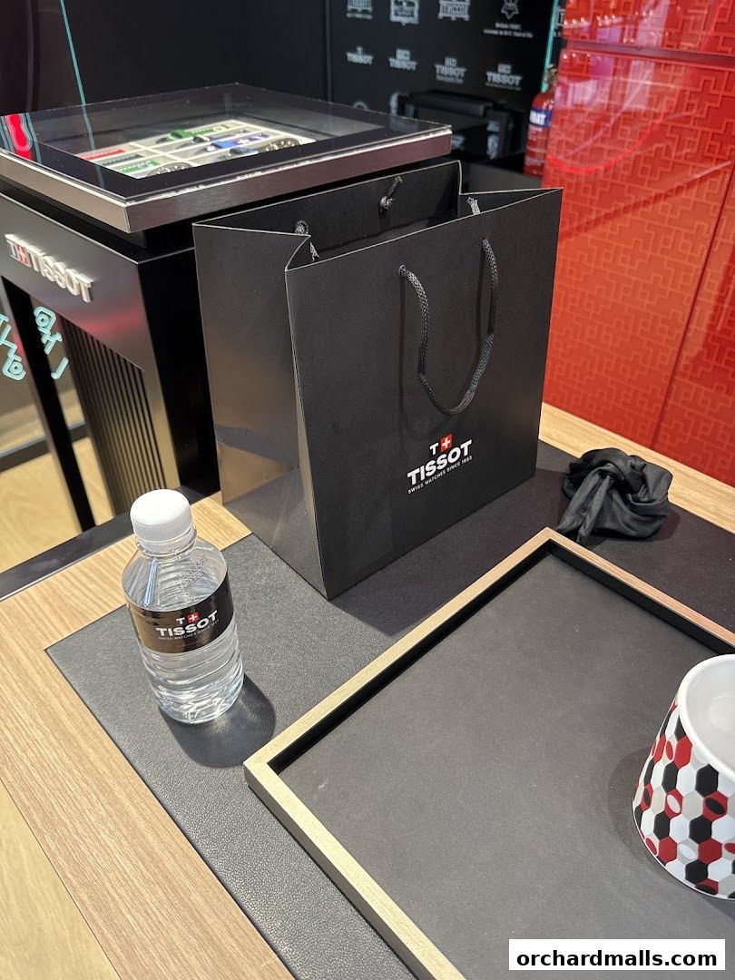 A Tissot shopping bag, water bottle, and display case with watches on a counter.