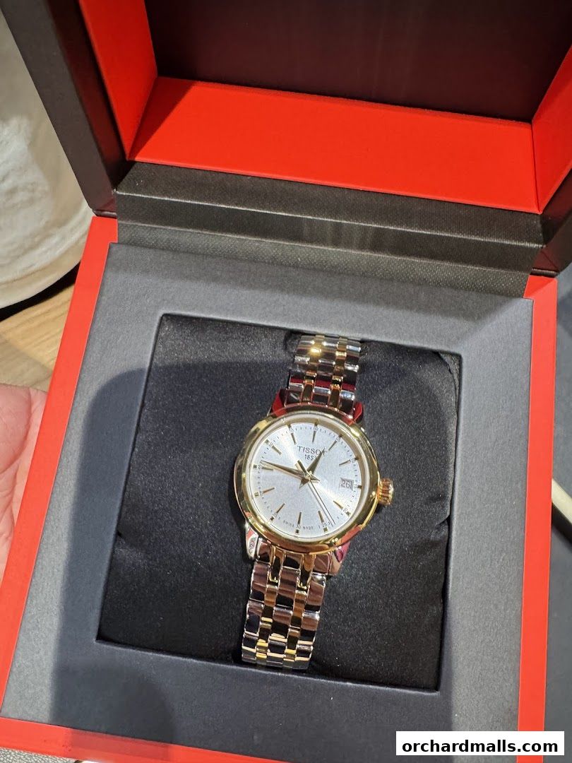 A Tissot watch with a silver dial and gold accents, presented in its red and black box.