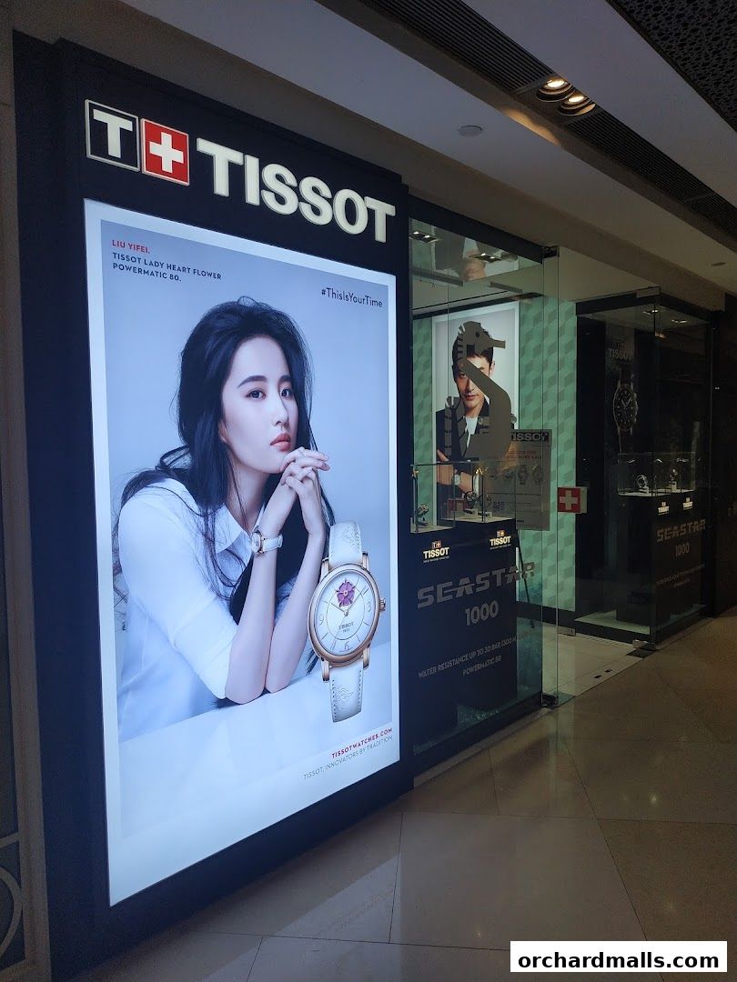 The Tissot shop front features a large illuminated advertisement with a model and a watch, alongside the store entrance.