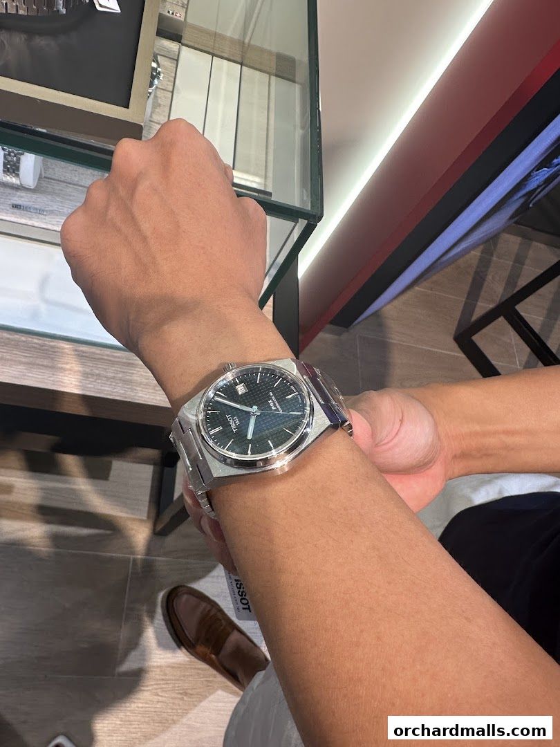 A person tries on a Tissot watch inside a well-lit retail store.