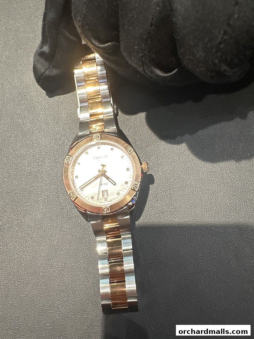 A Tissot watch with a two-tone metal band is held by a gloved hand.