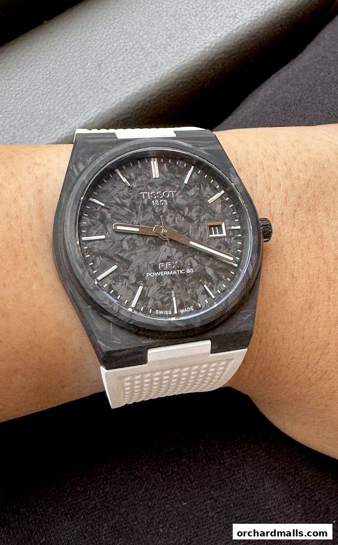 A close-up shot of a Tissot watch with a textured black dial and white strap on a wrist.