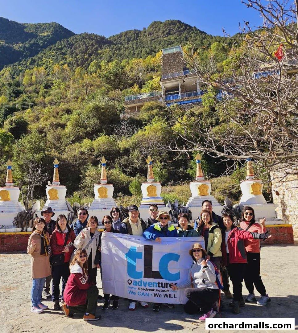 A group of tourists poses with a banner in front of stupas and a building on a hillside.