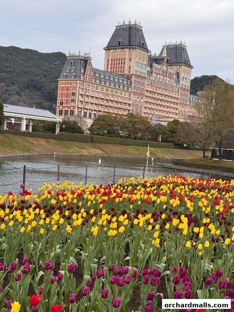 A grand hotel building overlooks a vibrant field of tulips and a calm body of water.