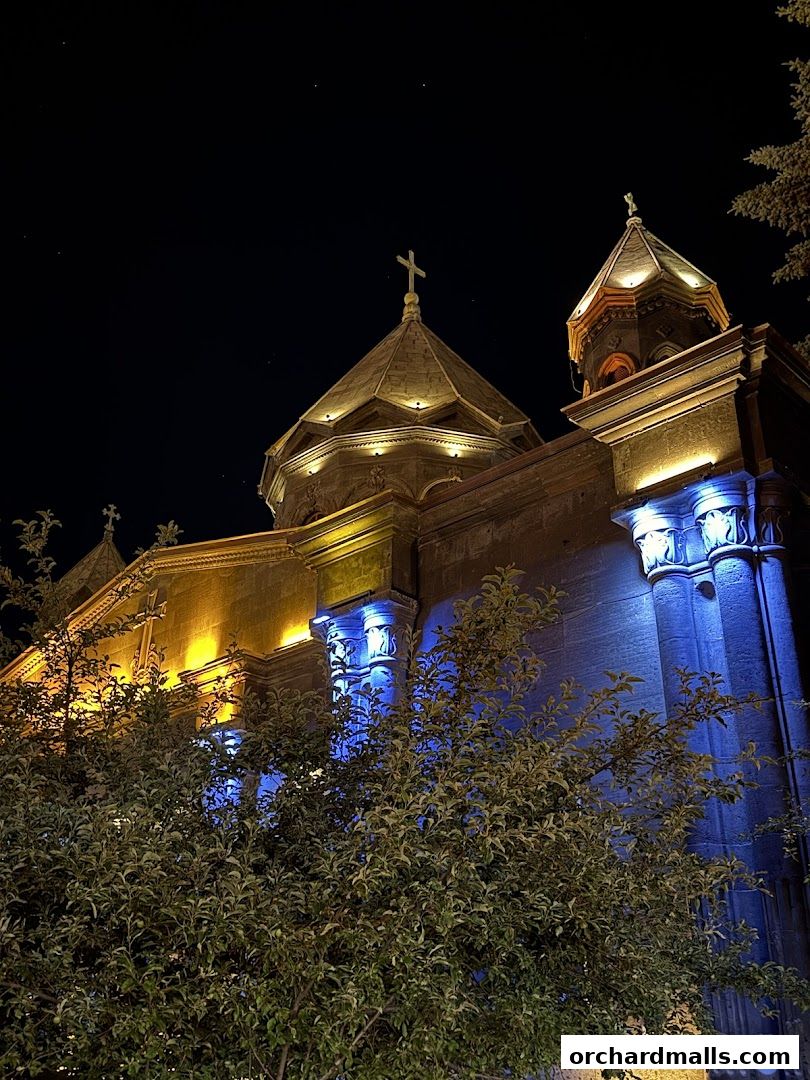 A stone building with crosses on domes, illuminated by yellow and blue lights at night.