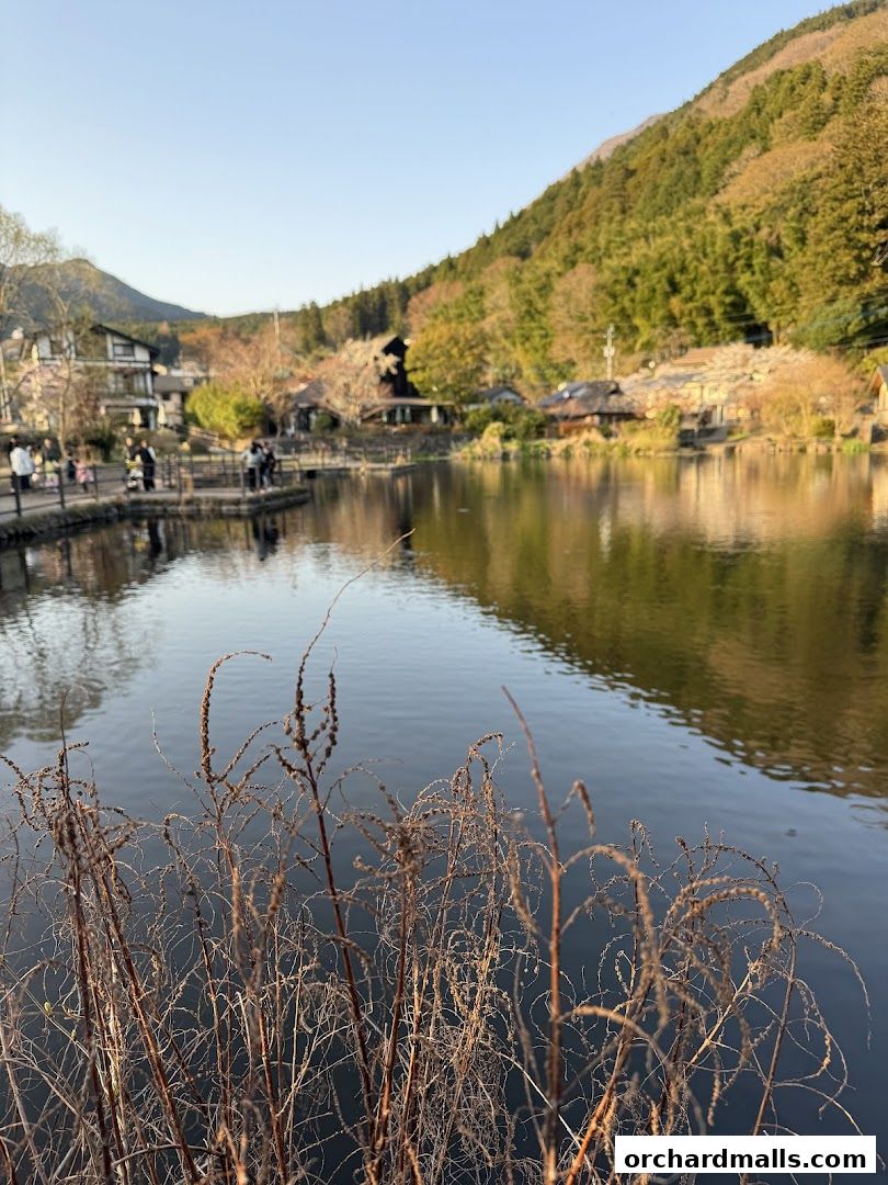 A serene lake with traditional buildings and lush green hills in the background.