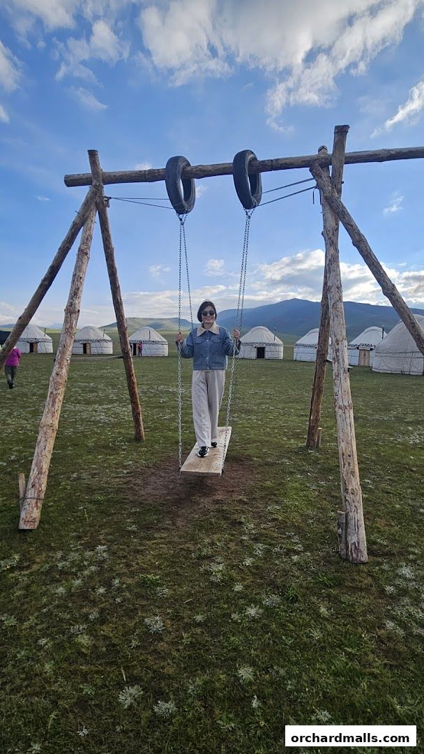 A woman on a swing in front of traditional yurts under a cloudy sky.