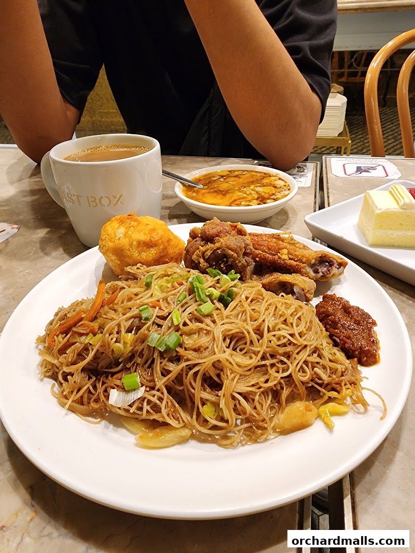 A plate of noodles with fried chicken, a fried bun, and a side dish, with a cup of coffee.