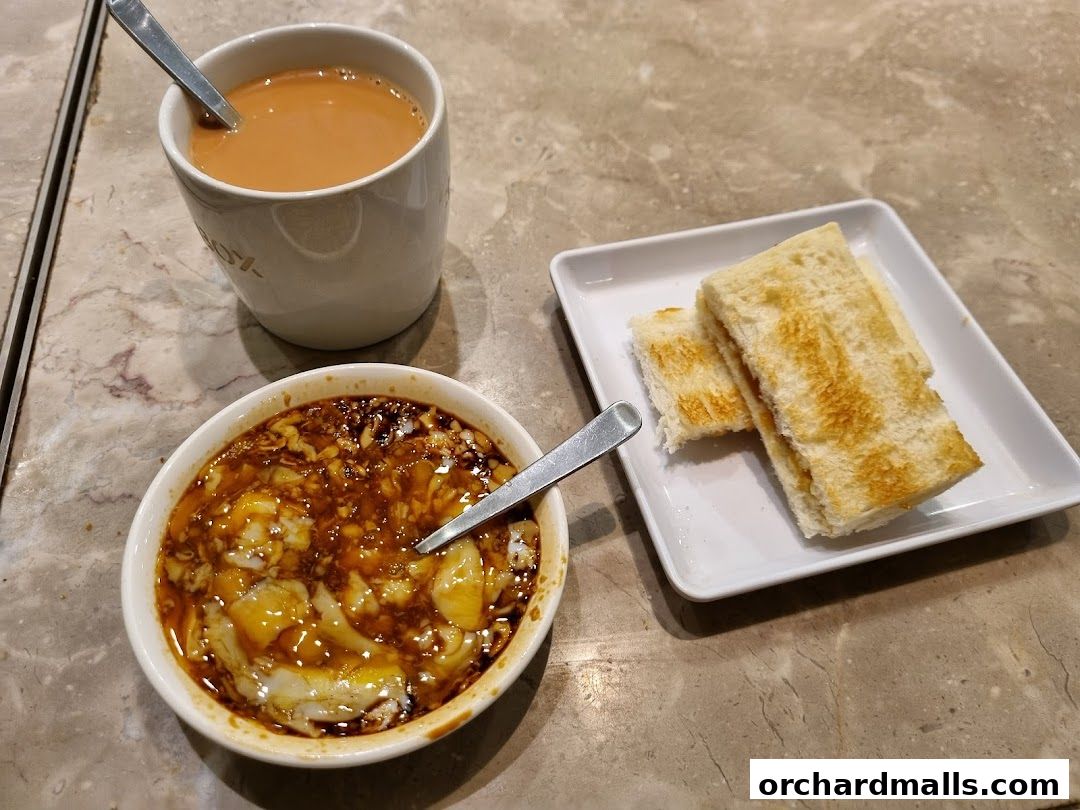 A close-up of a traditional Singaporean breakfast with soft-boiled eggs, toast, and milk tea.