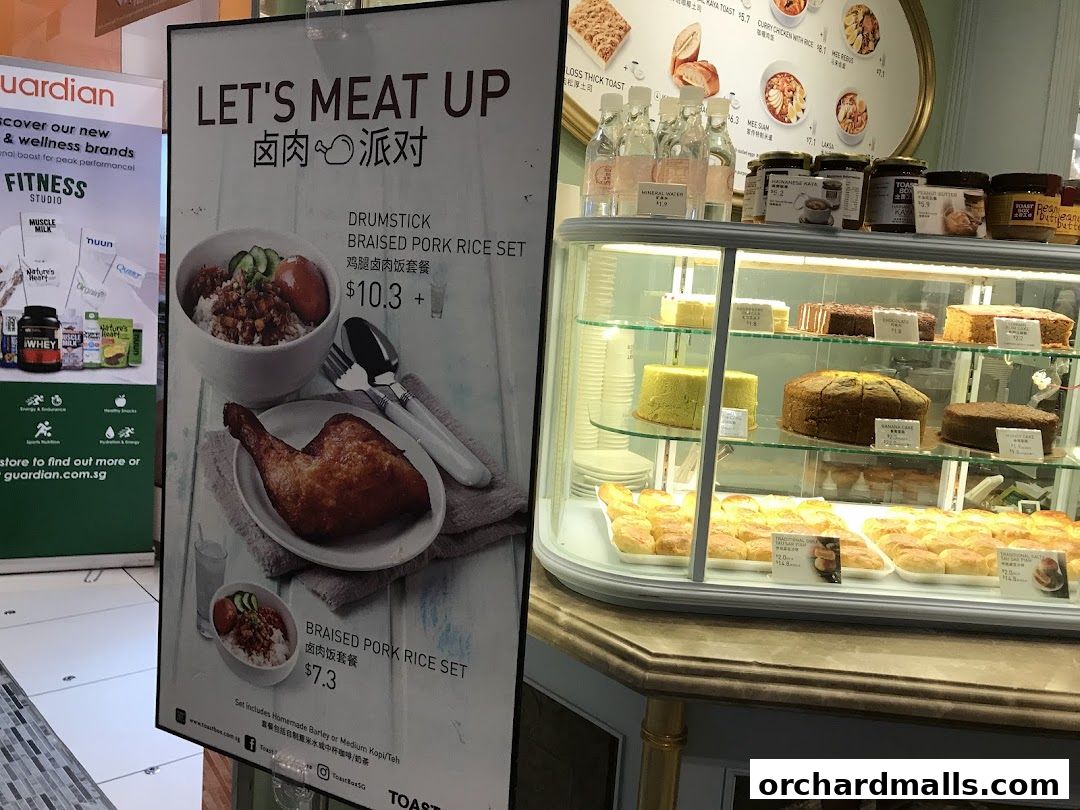 A sign advertising a braised pork rice set next to a display of cakes and pastries.