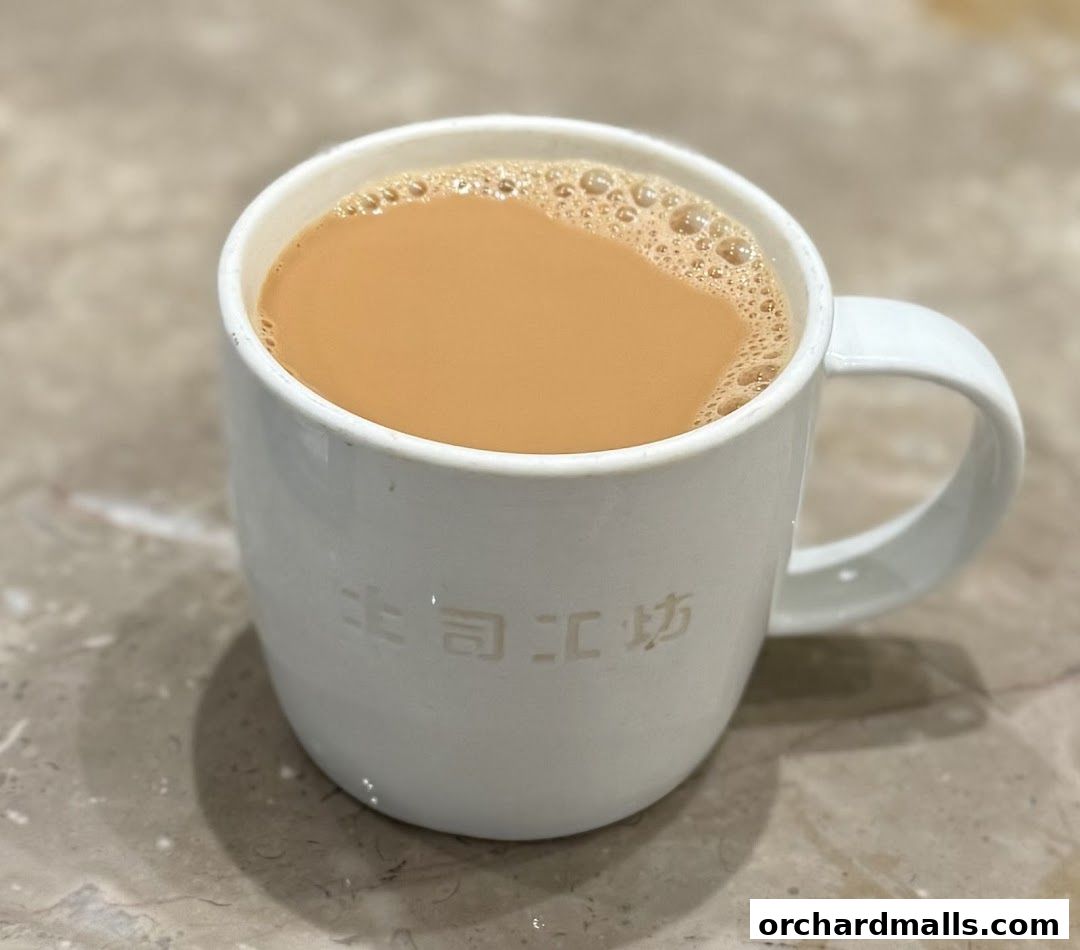 A close-up shot of a white mug filled with frothy, milky tea.