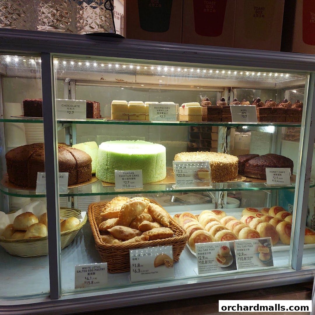 A display case filled with various cakes, pastries, and buns from Toast Box.