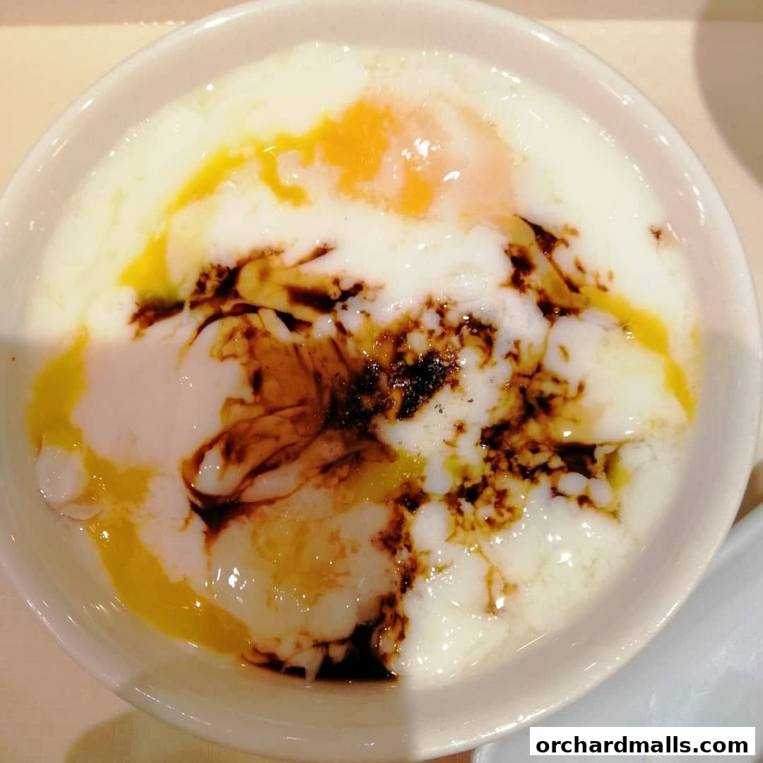 A close-up shot of soft-boiled eggs drizzled with soy sauce and pepper in a white bowl.