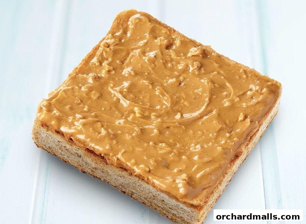 A slice of toast generously spread with creamy peanut butter and crunchy peanut pieces.