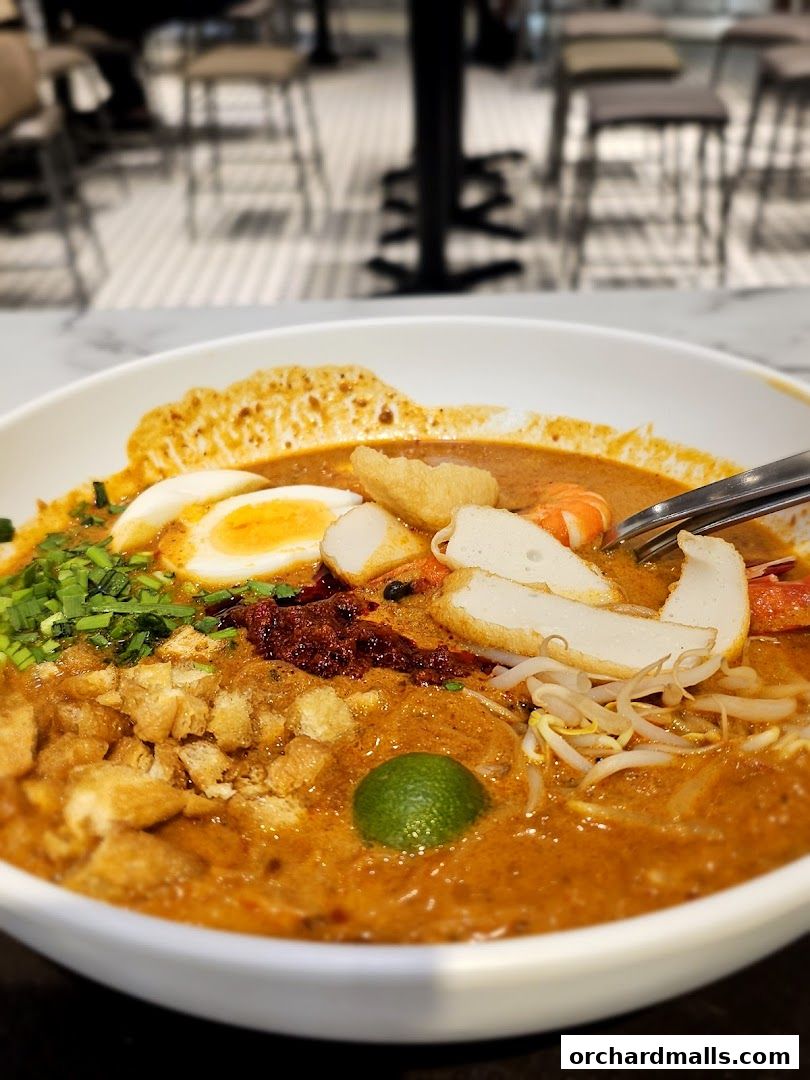 A close-up of a delicious bowl of Laksa with various toppings and a lime wedge.